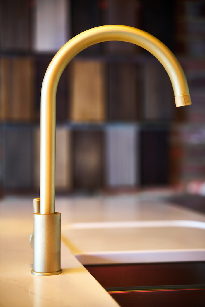 A brushed gold tap on a white countertop.