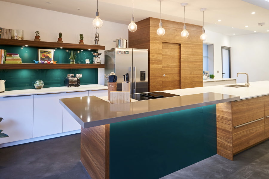 A colourful, modern kitchen with white and wooden cabinetry, a spacious island with in-built hob and sink, and stylish exposed bulb pendant lights.