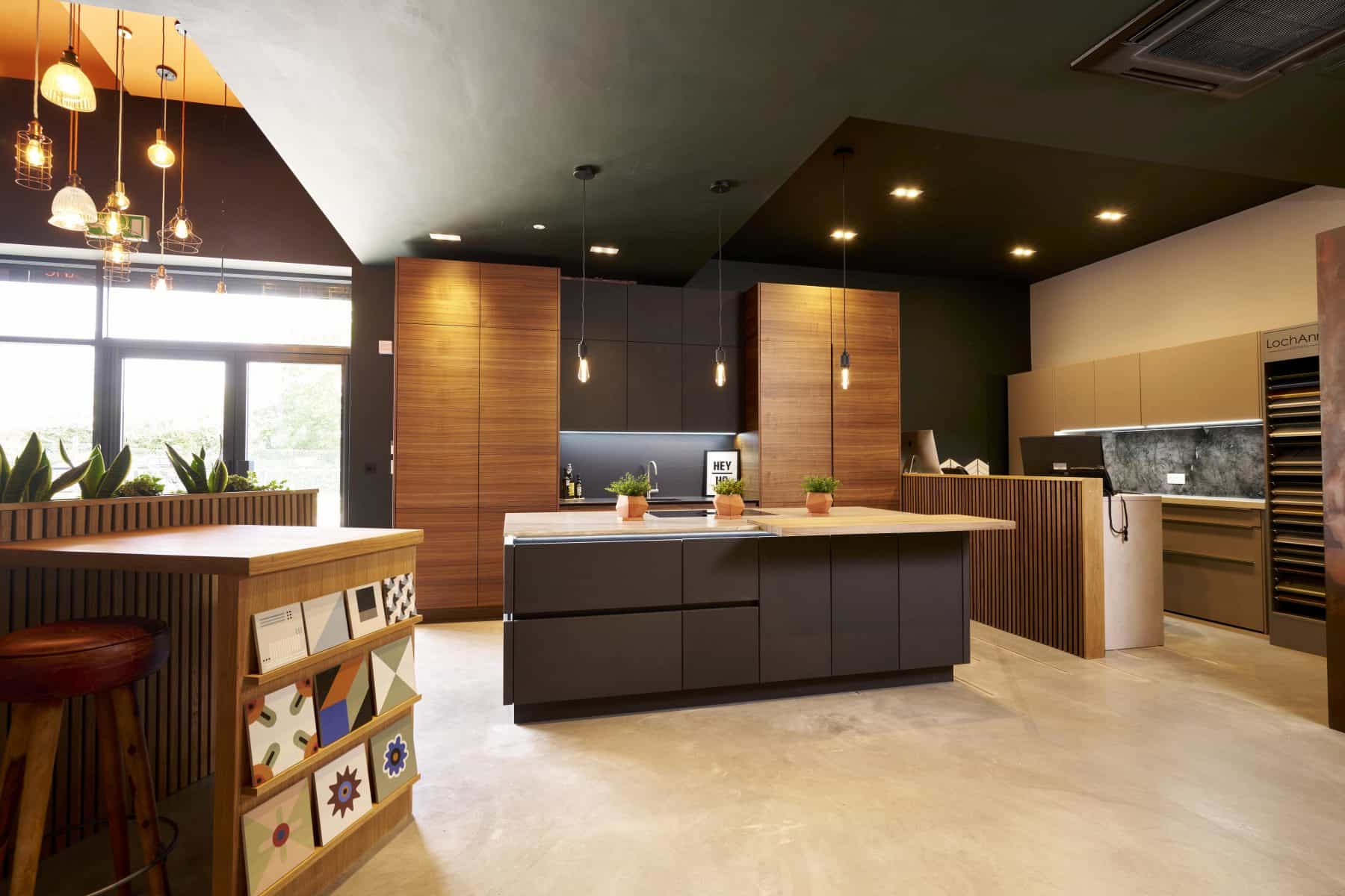 Contemporary kitchen with a mix of dark grey and wooden cabinets, and a spacious island that is illuminated by pendant lights.
