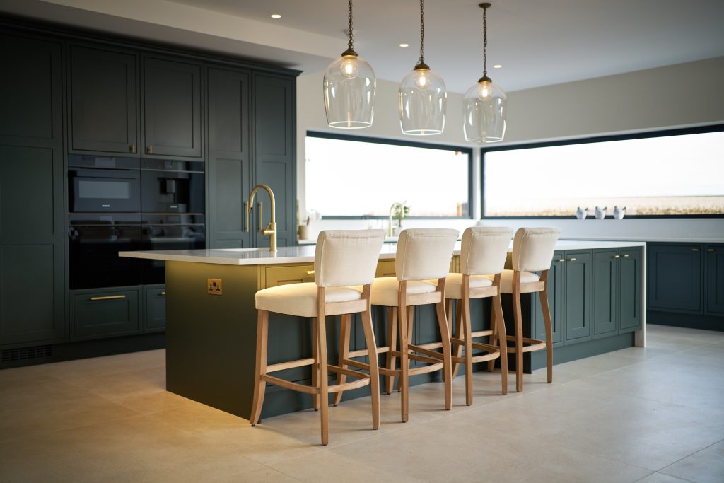 Modern kitchen with dark green shaker cabinets, a large island, and sleek bar stools, featuring pendant lights.