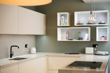 A minimalist kitchen featuring light cabinetry, a black faucet, and open shelving with decorative items.